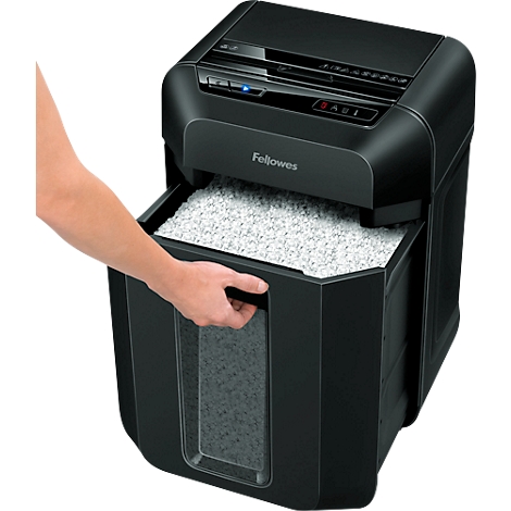 A person opening a black paper shredder drawer filled with shredded paper. The "Fellowes" logo is visible.