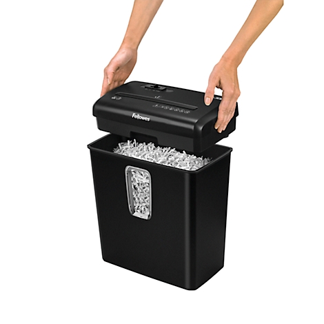 Shredder top being lifted by hands, filled with shredded paper. Black waste bin.