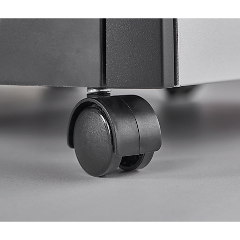 Close-up of a black caster wheel attached to a piece of furniture. The background is blurred and gray.