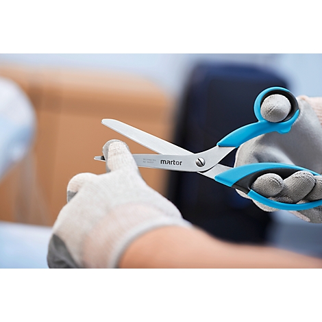 Nahaufnahme von Scheren, die eine kleine Spitze schneiden. Die Schere hat blaue Griffe und den Schriftzug "martor". Hände tragen Handschuhe.