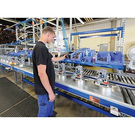 Ein Mann arbeitet an einem Fließband in einer Fabrik. Er betrachtet ein montiertes Gerät.