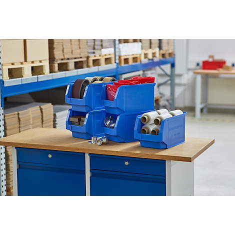 Blaue Kisten mit verschiedenen Materialien auf einem Holztisch vor einem Lagerregal. Kisten sind mit Rollen, Bändern und anderen Gegenständen gefüllt.