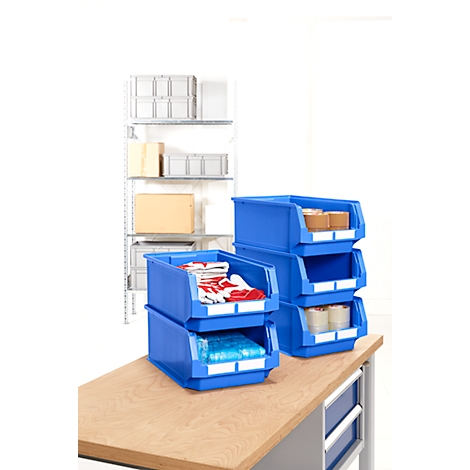 Blaue Lagerboxen mit Inhalten wie Handschuhen und Rollen auf Holztisch. Im Hintergrund Regale mit Kisten.