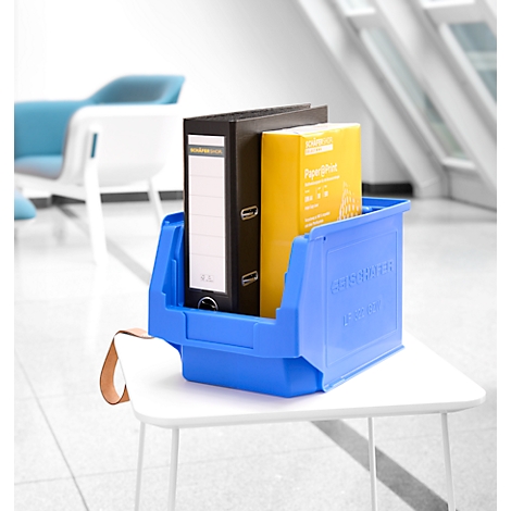 Blaue Sichtlagerbox auf einem weißen Tisch, gefüllt mit einem schwarzen Ordner und gelben Papier.