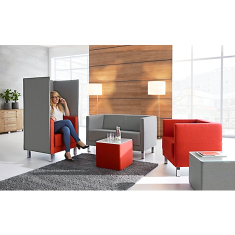A woman talking on the phone in a red armchair, inside a grey room divider, other furniture is present.