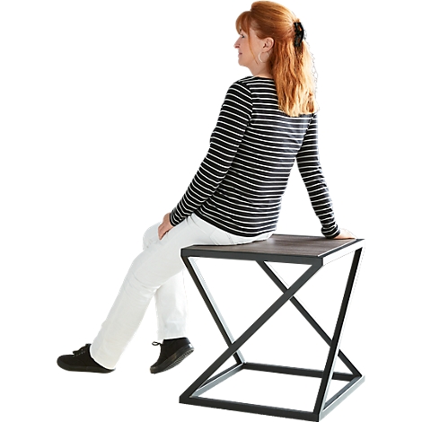 Woman sitting on square side table with black metal frame. She wears striped shirt, white trousers.