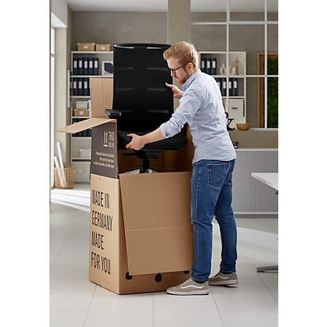 Un homme assemble une chaise de bureau noire à partir d'un carton. Le carton porte l'inscription "Made in Germany".