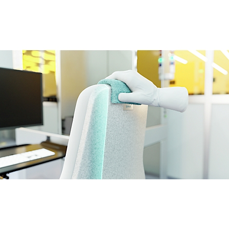 Une main blanche gantée essuie le dossier d'une chaise blanche avec un chiffon turquoise.