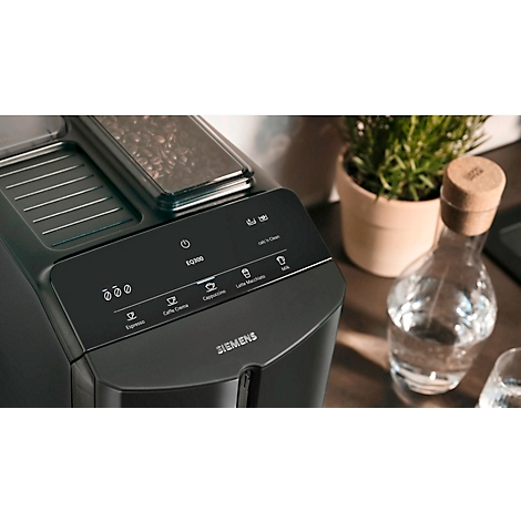 Nahaufnahme eines schwarzen Kaffeevollautomaten. Bedienfeld mit Tasten für Espresso, Cappuccino, Latte Macchiato, etc.. Im Hintergrund: Vase mit Wasser.