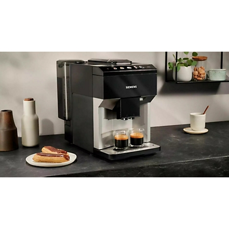 Eine schwarze Kaffeemaschine mit zwei Espressogläsern. Auf dem Tisch stehen Gebäck, eine Tasse und Dekorationsartikel.