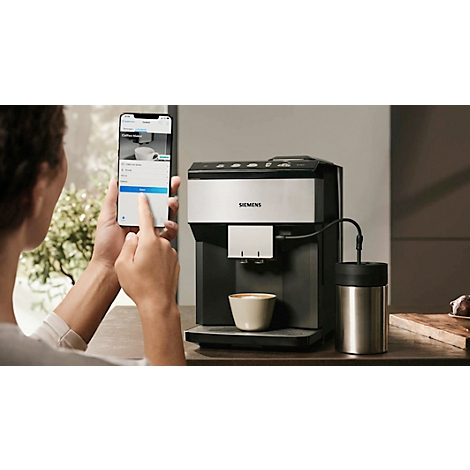 Person mit Smartphone bedient Kaffeemaschine mit Cappuccino in Tasse.