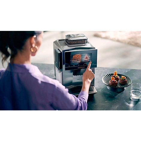 Une personne utilise une machine à café, l'écran affiche des options de café. Des pâtisseries sur une assiette sont sur le côté.