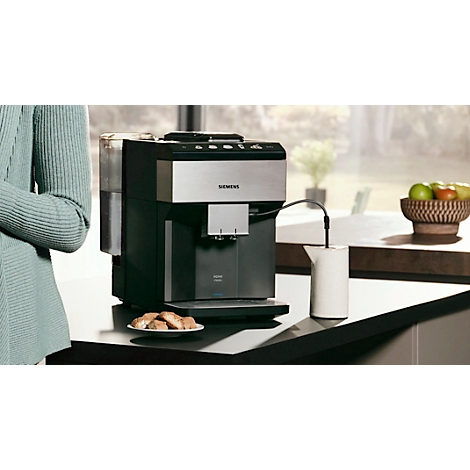 Koffiemachine op een aanrecht. Naast de machine staan een kan, een bord met gebak en een fruitschaal.