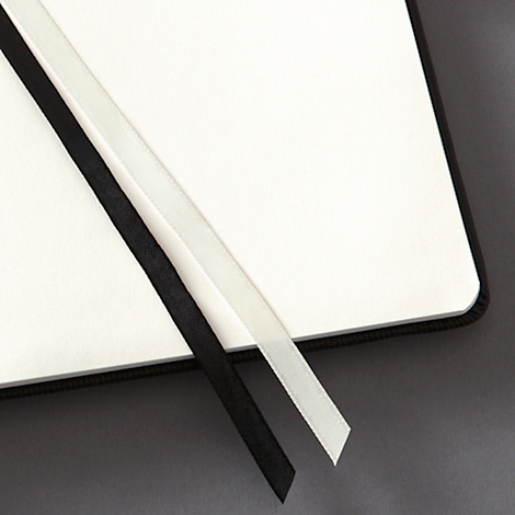 Gros plan sur un carnet ouvert. Marque-pages noir et blanc sur les pages blanches.