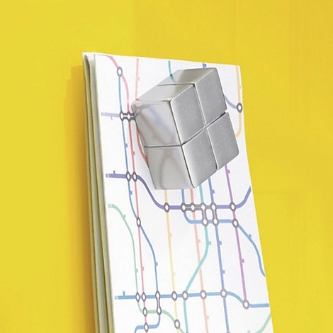 Aimant argenté en forme de cube sur un bloc-notes avec une carte du métro, sur fond jaune.