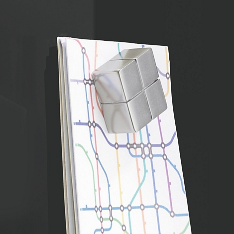 Zilveren kubusmagneet op een notitieboekje met een metrokaart.