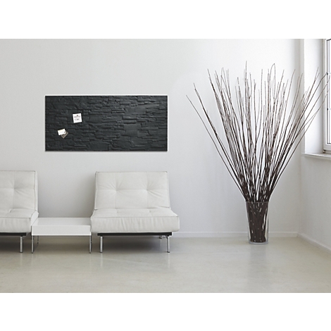 Ein schwarzes Wandboard mit Notizen, zwei weiße Sofas, eine Vase mit Zweigen und ein Fenster.