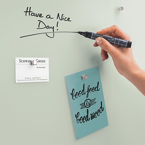 Eine Hand, die mit einem schwarzen Marker "Have a nice day!" auf eine helle Tafel schreibt. Auf der Tafel hängen Notizen.