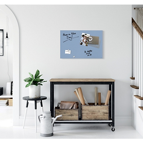 Blaues Whiteboard mit Notizen und Fotos an der Wand. Darunter ein Holztisch mit Deko.