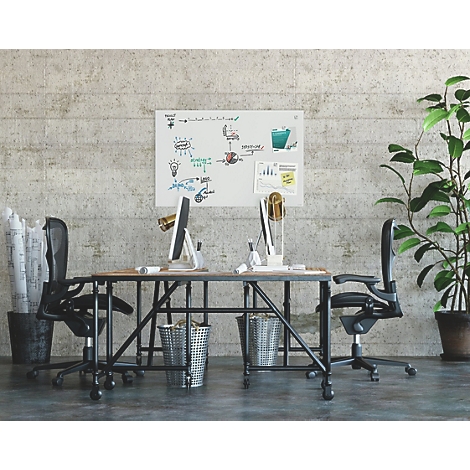Büro mit zwei Schreibtischen, Stühlen und einem Whiteboard mit Skizzen an einer Betonwand. Eine Topfpflanze steht daneben.