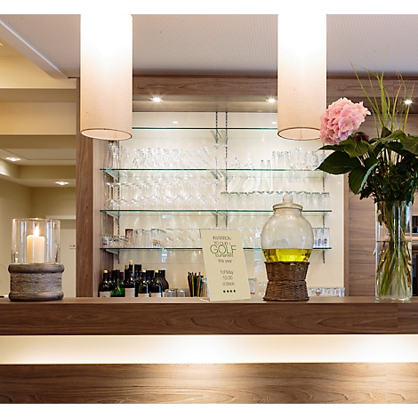 Vue d'un bar avec des lampes décoratives et des fleurs. Des verres sont sur des étagères en verre en arrière-plan.