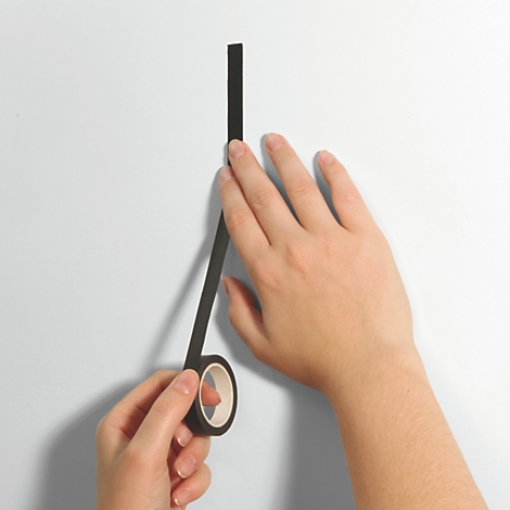 Hände kleben einen schwarzen Streifen Klebeband an eine weiße Wand. Klebebandrolle in der unteren Hand.