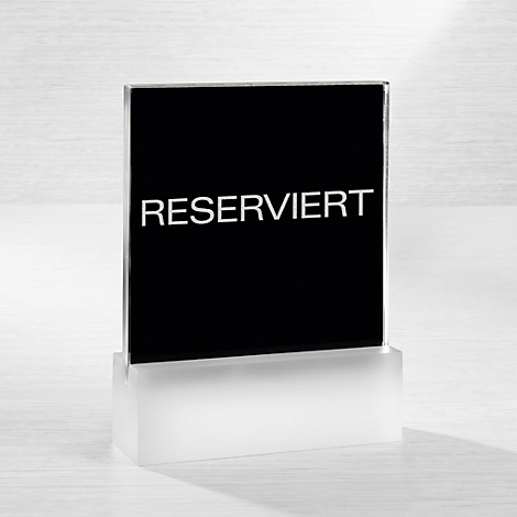 Ein schwarzes Aufstellschild mit der weissen Aufschrift RESERVIERT auf einem milchig-transparenten Sockel.