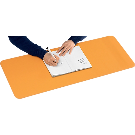 Person schreibt mit Stift in Notizbuch, das auf orangefarbener Schreibtischunterlage liegt.