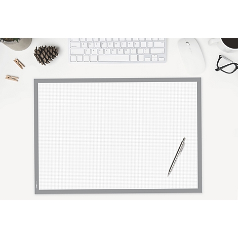 Draufsicht auf einen Schreibtisch mit karierter Schreibunterlage, Tastatur, Maus, Brille, Stift und Deko-Elementen.