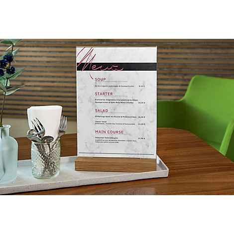 Menu card on a wooden stand. Various cutlery in a glass, white napkin paper and a green chair in the background.