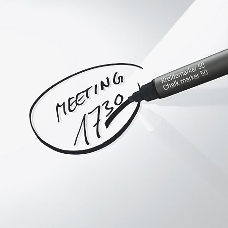 Un stylo noir écrit sur une surface blanche. Il écrit "Meeting 1730" dans une forme ovale. Le stylo indique "Kreidemarker 50".