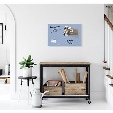 Tableau mémo bleu clair avec notes et photos sur le mur. En dessous, une table avec décoration et une plante.