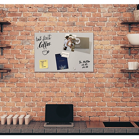 Vue d'un mur de briques avec un tableau d'affichage gris attaché. Le tableau d'affichage contient des notes, des photos et un ordinateur portable.