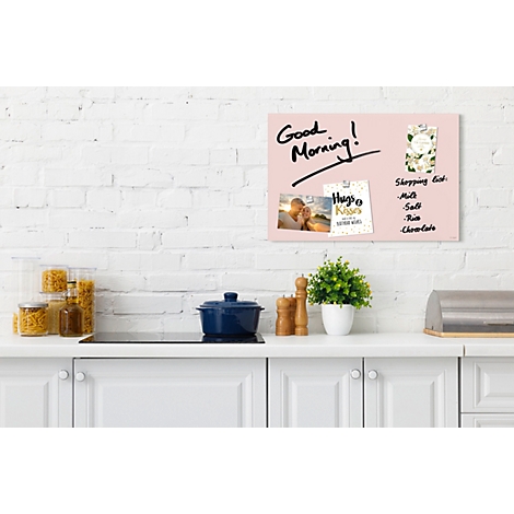 Tableau magnétique rose avec des notes et 'Good Morning'. Dans une cuisine, sur une surface blanche, avec des accessoires.