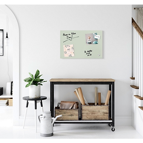 Tableau magnétique vert clair avec des notes et des photos sur le mur. En dessous, une table avec décoration et escalier.