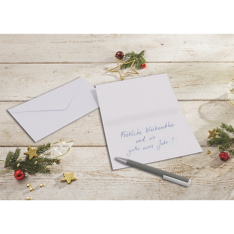 Eine geöffnete Weihnachtskarte mit handgeschriebenem Text liegt neben einem Umschlag und einem Kugelschreiber auf einem Holztisch.