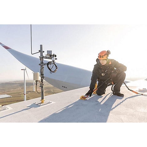 Un travailleur est agenouillé sur une éolienne et travaille. Il porte un casque et est attaché avec une corde.