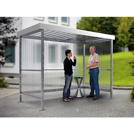 Two men stand under a shelter. One man points upwards, they seem to be talking to each other.