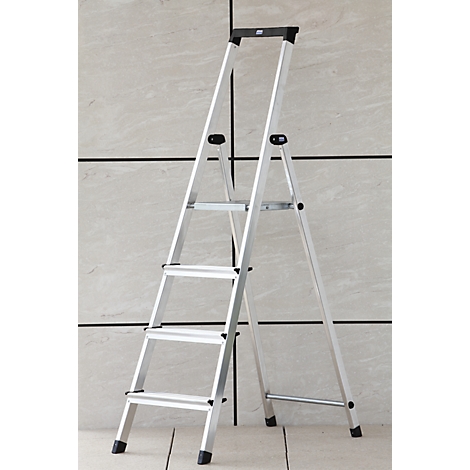 A silver step ladder stands in front of a light gray wall. Four steps, black feet.