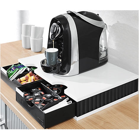 Coffee machine in action, black design, cup filling. Drawers with capsules and snacks. White shelf, wooden table.