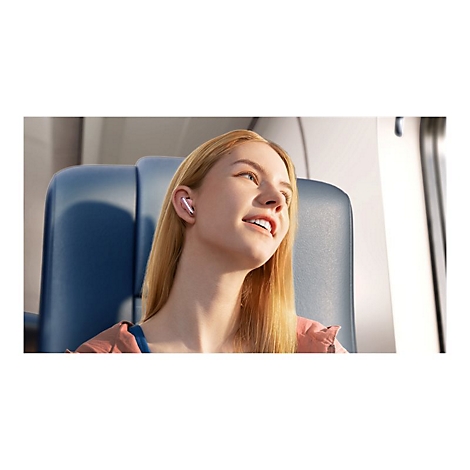 Junge Frau im Flugzeug mit Ohrhörer. Sie lächelt und schaut nach oben rechts.