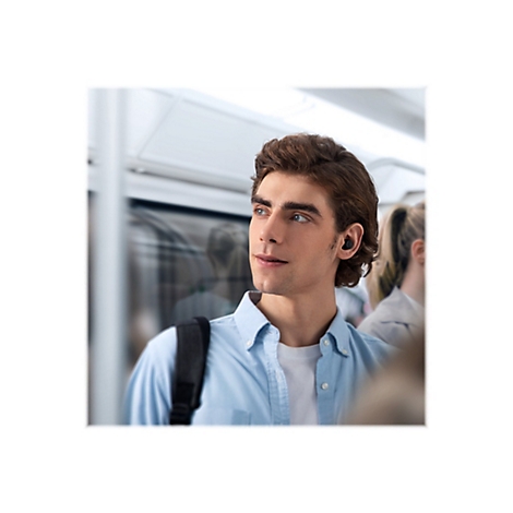 Ein junger Mann mit Kopfhörern in einem Zug. Er trägt ein blaues Hemd und schaut aus dem Fenster.