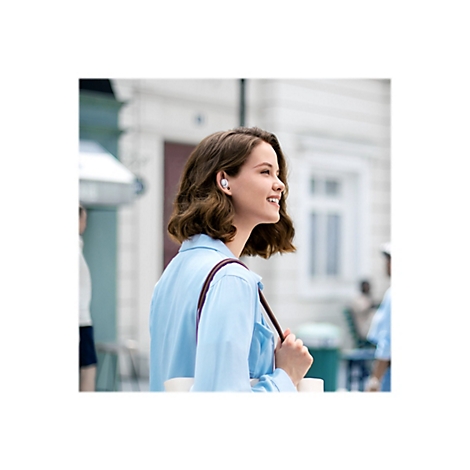 Eine Frau trägt Kopfhörer und lächelt draußen, Sonnenlicht.