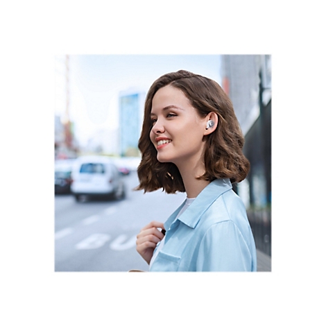 Junge Frau lächelt mit Kopfhörern im Ohr; im Hintergrund Stadtverkehr.