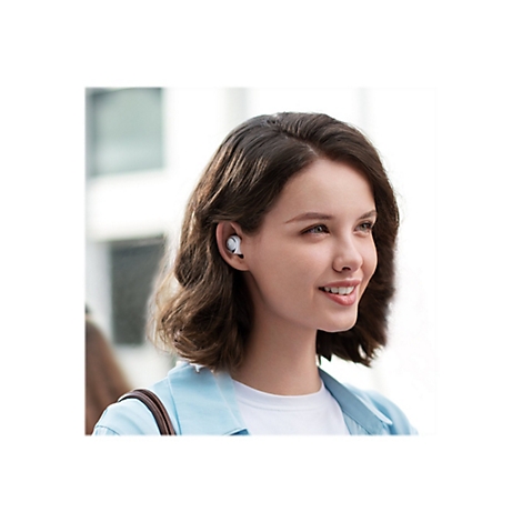 Eine junge Frau mit braunen Haaren und einem Ohrhörer lächelt. Sie trägt eine helle Jacke.