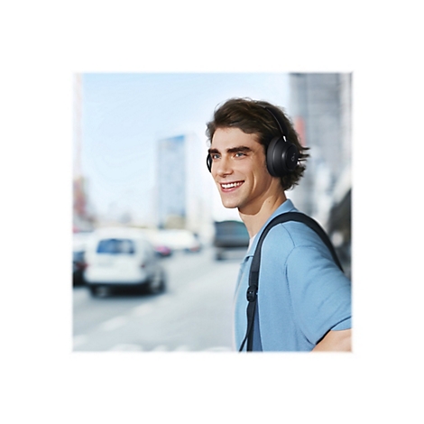 Ein lÃ¤chelnder Mann mit KopfhÃ¶rern Ã¼berquert die StraÃŸe. Er trÃ¤gt einen Rucksack und ein blaues Hemd.