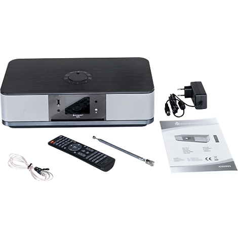 Grijze radio met afstandsbediening, voeding, antenne en handleiding op een witte achtergrond.