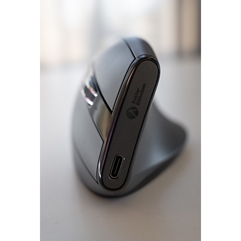 Souris ergonomique grise avec texte "Bakker Elkhuizen". Port USB-C, posé sur une surface claire.