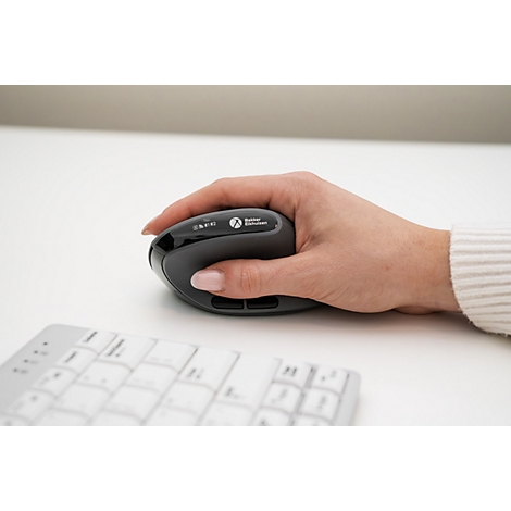 Main tenant une souris ergonomique grise, clavier au premier plan.