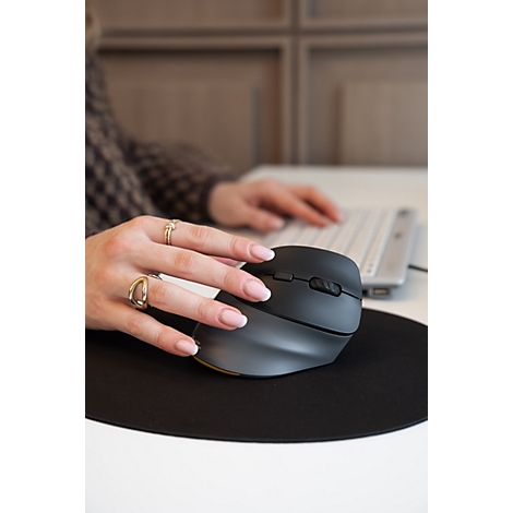Main actionnant une souris verticale ergonomique noire sur un tapis de souris rond noir.